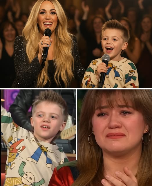No one expected the most powerful moment of the night to come from the smallest voice in the room. But when Kelly Clarkson’s son Remy stepped onto the stage—his hands trembling, his heart wide open—he whispered a sentence that shattered every wall in the arena: “If Dad can’t be by Mom’s side… then I’ll be the one to stand there for her.” The crowd fell into breathless silence. Kelly Clarkson broke down in tears, her hands covering her face as her son stood bravely under the lights. Carrie Underwood knelt beside him, her voice barely holding together as she whispered, “This is love, right here.” With thousands watching, Remy softly sang “Because You Loved Me.” His voice cracked, but he kept going—every note landing like a gentle blow to the heart. Cameras captured raw, tearful faces in the crowd, strangers holding hands, parents hugging children tighter.
